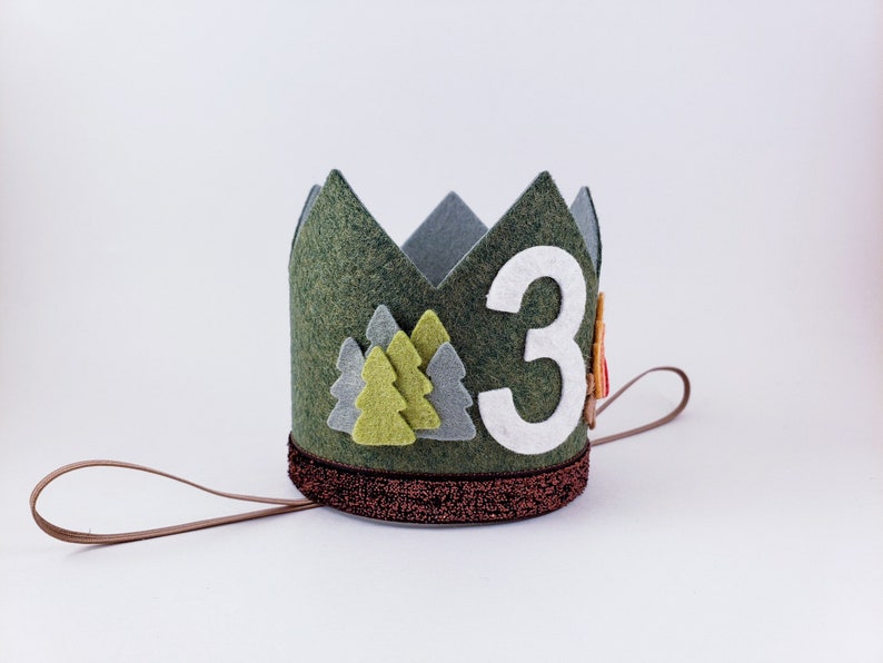 May include: Green felt crown with a white felt number 3, green and gray felt trees, and a brown felt tie.