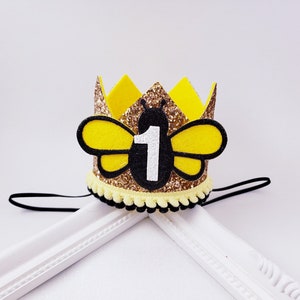 May include: Gold glitter bee crown with a yellow felt bee and the number 1 in white. The crown has a black elastic band.