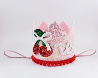 May include: Pink felt crown with a red and green glitter cherry, white glitter letters spelling "one", and a red pom-pom trim.