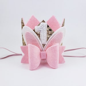 May include: Pink felt headband with a gold glitter crown, white felt bunny ears, and a pink bow. The crown has a white felt number one on it.