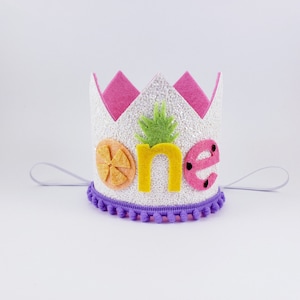 May include: White felt crown with a pink felt top and purple pom pom trim. The crown has the word "one" in yellow felt letters with a pineapple, orange slice, and watermelon applique.