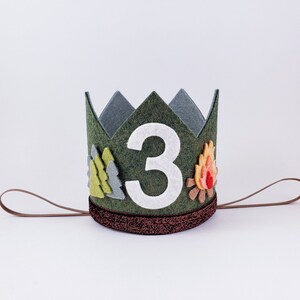 May include: A green felt crown with a white felt number "3" in the center. The crown is decorated with felt trees and a campfire. The crown has a brown felt tie.