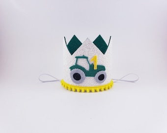 May include: White felt crown with a green tractor and the number 1 on it. The crown has a yellow pom-pom trim.