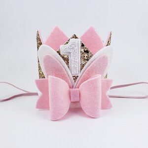 May include: Pink felt headband with a gold glitter crown, white felt bunny ears, and a pink bow. The crown has a white felt number one on it.