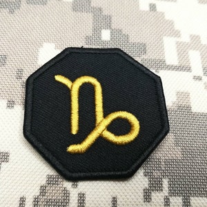 Op de afbeelding: Zwarte achteckige patch met een gouden geborduurd sterrenbeeld Steenbok.