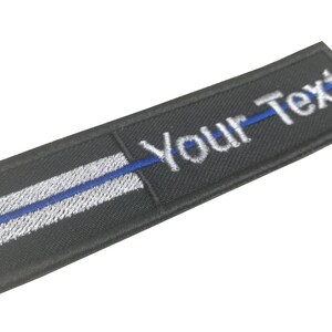 May include: Black embroidered patch with a thin blue line and white border. The text "Your-Text" is embroidered in white.