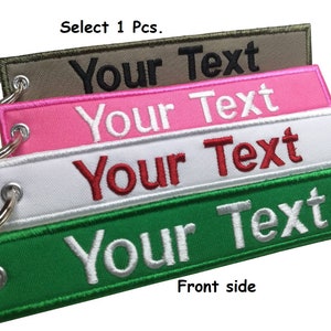 Puede incluir: Cuatro llaveros con diferentes correas de tela de colores y anillos de metal. Las correas son verdes, blancas, rosas y marrones. Cada correa tiene el texto "Your Text" bordado en ella en un color contrastante. El texto "Select 1 Pcs." está en la parte superior de la imagen y "Front side" está en la parte inferior.