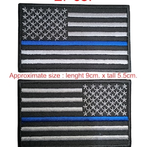 Könnte beinhalten: Zwei gestickte Aufnäher mit der amerikanischen Flagge und einer dünnen blauen Linie. Die Aufnäher sind schwarz mit weißen Sternen und Streifen und einer blauen Linie in der Mitte. Die Aufnäher sind etwa 9 cm lang und 5,5 cm hoch.