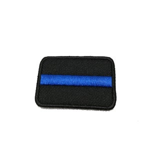 Könnte beinhalten: Schwarzer gestickter Aufnäher mit einem dünnen blauen Streifen in der Mitte. Der Aufnäher ist rechteckig und hat einen schwarzen Rand.
