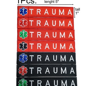 Op de afbeelding: Zeven geborduurde patches met het woord "TRAUMA" in witte letters op een rode of zwarte achtergrond. Elke patch heeft een ander gekleurd medisch symbool met een slang en een staf. De patches zijn 2,5 cm hoog en 12,7 cm lang.