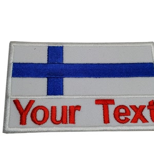 Puede incluir: Parche blanco bordado con la bandera de Finlandia y el texto "Your Text" en rojo.
