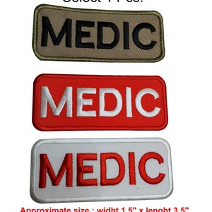 May include: Three embroidered patches with the word "MEDIC" in different colours. The patches are beige with black lettering, red with white lettering, and white with red lettering. The patches are approximately 1.5 inches wide and 3.5 inches long.