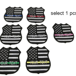 May include: Eight embroidered patches featuring the American flag with a thin line in different colors. The patches are shaped like a shield and have the text "YOUR TEXT" on them.  Select 1 pcs.