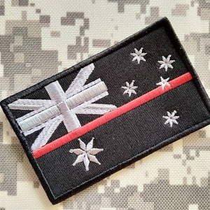 May include: A black embroidered patch featuring a white Southern Cross and a red stripe. The patch is displayed against a camouflage background.