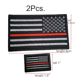 Może przedstawiać: Dwa haftowane naszywki z amerykańską flagą z cienką czerwoną linią. Większa naszywka ma 5,5 cm wysokości i 9 cm szerokości. Mniejsza naszywka ma 1 cal wysokości i 1,5 cala szerokości.
