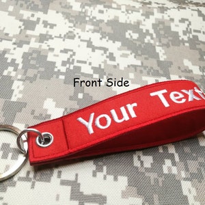 May include: Red fabric keychain with a white metal ring and the text "Your Text" embroidered in white.