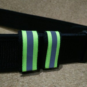May include: Black belt with two green and gray reflective strips. The strips are sewn onto the belt.