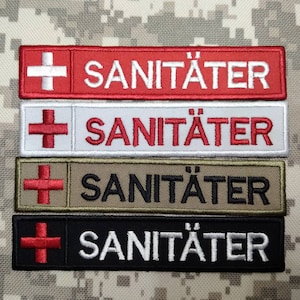 May include: Four embroidered patches with the word "SANITÄTER" and a red cross. The patches are in different colors: red, white, khaki, and black.