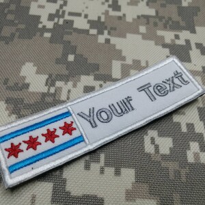Op de afbeelding: Witte geborduurde patch met een blauwe en witte vlag met rode sterren en de tekst "Your Text" in grijs.