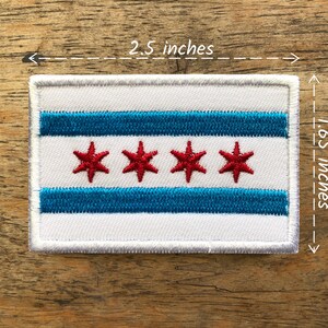 May include: White embroidered patch with the Chicago flag. The flag has three horizontal blue stripes and four red stars on a white background. The patch measures 2.5 inches by 1.65 inches.
