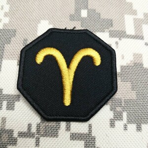May include: A black and gold embroidered patch with the astrological symbol for Aries, a ram's horns.
