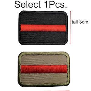 Könnte beinhalten: Zwei gestickte Patches mit einem roten Streifen auf schwarzem Grund und einem roten Streifen auf beigefarbenem Grund. Die Patches sind 4,5 cm lang und 3 cm hoch. Wählen Sie 1 Stück.