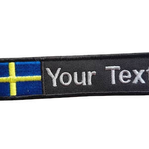 May include: Black embroidered patch with the Swedish flag on the left and the text "Your Text" on the right.