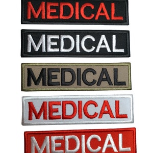 Pode incluir: Cinco patches bordados com a palavra "MEDICAL" em diferentes combinações de cores. Os patches são pretos, vermelhos, brancos e bege. O texto é branco sobre vermelho, vermelho sobre branco, branco sobre preto e preto sobre bege. Os patches medem aproximadamente 2,5 cm de largura e 10 cm de comprimento.