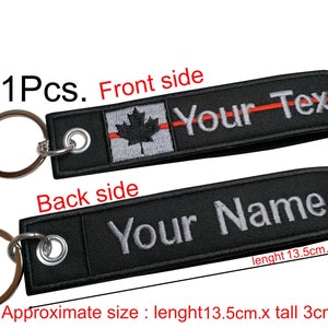 May include: A black key chain with a red and white Canadian flag and the text "Your Text" on the front side. The back side has the text "Your Name". The key chain measures approximately 13.5 cm long and 3 cm tall.