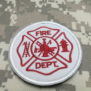 Pode incluir: Etiqueta branca bordada com um logotipo vermelho do departamento de bombeiros. O logotipo apresenta um hidrante, uma escada, um machado e uma mangueira. O texto "FIRE DEPT" está escrito em vermelho.