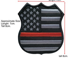 Può includere: Un patch di bandiera americana in bianco e nero con una striscia rossa al centro. Il patch ha la forma di uno scudo e misura circa 7 cm di lunghezza e 8 cm di altezza.