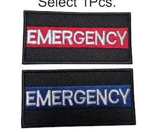 Può includere: Due toppe ricamate nere con la parola "EMERGENCY" in lettere bianche. La toppa superiore ha una striscia rossa e la toppa inferiore ha una striscia blu. Le toppe sono lunghe circa 10 cm e alte 5 cm.