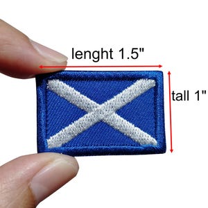 Op de afbeelding: Een rechthoekige blauwe patch met een wit kruisvormig ontwerp, dat op een vlag lijkt. De patch is 3,8 cm lang en 2,5 cm hoog. De tekst "lenght 1.5" en "tall 1" zijn zichtbaar op de afbeelding.