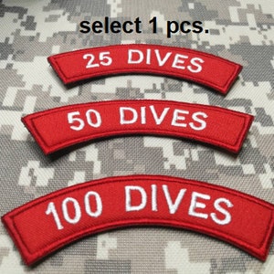 Peut inclure: Trois patchs brodés rouges avec du texte blanc. Les patchs sont en forme d'arche et indiquent "25 DIVES", "50 DIVES" et "100 DIVES".