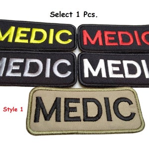 Könnte beinhalten: Fünf verschiedene Stile von schwarzen gestickten Patches mit dem Wort "MEDIC" in verschiedenen Farben. Die Patches sind in gelber, roter, weißer, grauer und schwarzer Schrift erhältlich.