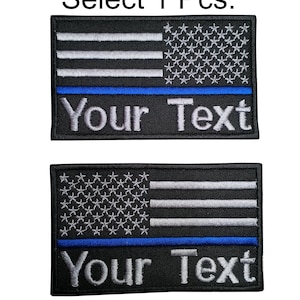 Könnte beinhalten: Zwei gestickte Aufnäher mit einer amerikanischen Flagge mit einem dünnen blauen Streifen und dem Text "Your Text" darunter. Die Aufnäher sind schwarz mit silbernen Sternen und Streifen und einem blauen Streifen.