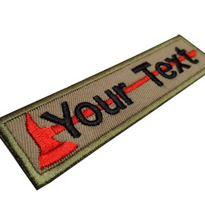 May include: An embroidered patch in tan and green with a red and black axe and the text "Your Text".