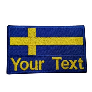 Peut inclure: Un patch brodé bleu et jaune avec le drapeau suédois et le texte "Your Text" en dessous.