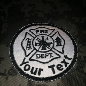 Puede incluir: Parche bordado blanco y negro con un símbolo de departamento de bomberos. El símbolo es una cruz con una escalera, una boca de incendios y un hacha. El texto "FIRE DEPT" está dentro de la cruz. El texto "Your Text" está debajo de la cruz.