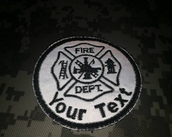 May include: White and black embroidered patch with a fire department symbol. The symbol is a cross with a ladder, a fire hydrant, and an axe. The text "FIRE DEPT" is inside the cross. The text "Your Text" is below the cross.