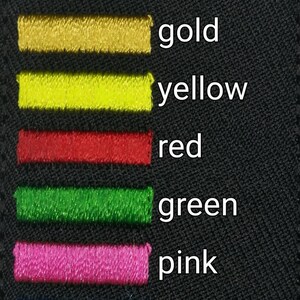 May include: A black fabric swatch with rows of colored thread samples. The colors are white, gray, gold, yellow, red, green, pink, light blue, and dark blue.