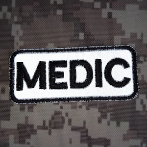 May include: White patch with black stitching and the word "MEDIC" in black lettering.