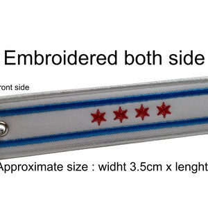 May include: White fabric keychain with a blue and red embroidered design of the Chicago flag. The text "Embroidered both side" and "Front side" are visible. Approximate size: 3.5 inches wide by 6 inches long.