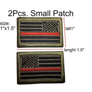 Pode incluir: Dois pequenos patches da bandeira americana com uma faixa vermelha no meio. Os patches medem 2,5 cm por 3,8 cm e são feitos de um tecido verde com um desenho de bandeira bordado em preto e branco.