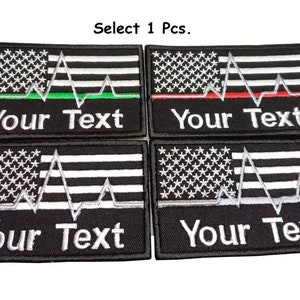 Könnte beinhalten: Vier gestickte Patches mit einer amerikanischen Flagge mit einer weißen Herzschlaglinie und dem Text "Your Text". Die Patches sind schwarz mit weißen und silbernen Stickereien. Die beiden oberen Patches haben jeweils eine grüne und eine rote Linie über der Herzschlaglinie.