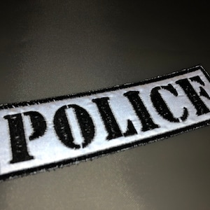 Może przedstawiać: Biała łatka z czarnym haftem z napisem "POLICE".