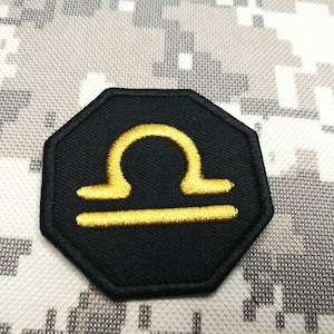 May include: Black fabric patch with a gold embroidered Libra zodiac symbol.