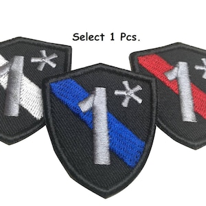 Puede incluir: Tres parches bordados en forma de escudo. Los parches son negros con una franja blanca, azul y roja en el centro. Cada parche tiene un número "1" plateado y un asterisco plateado.