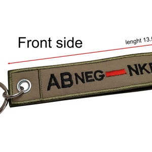 May include: A green key chain with a black embroidered text "ABNEG - NKDA" with a red line separating the words. The key chain is 13.5 inches long and 3 inches tall.