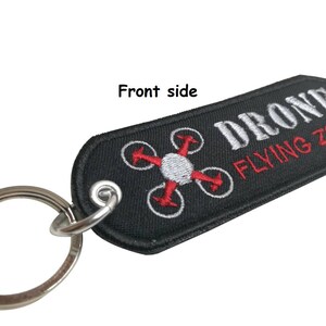 May include: Black key chain with a white embroidered drone symbol and the text "DRONE FLYING ZONE" in red.